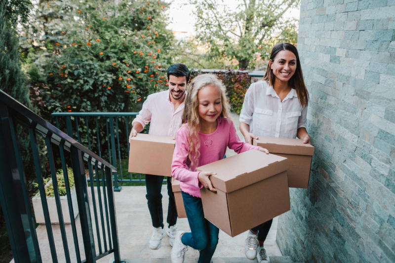 Smiling family carrying boxes into their new house