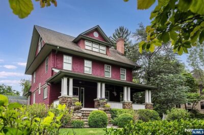 Large Craftsman-style home with a wraparound porch, mature landscaping, and a well-maintained front yard.