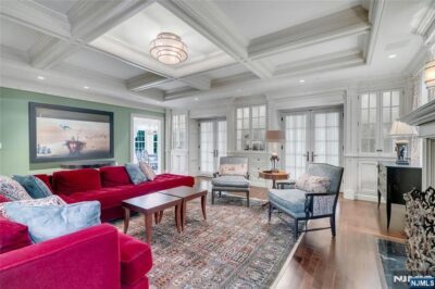 Spacious living room with coffered ceilings, built-in cabinetry, hardwood floors, and a traditional open layout.