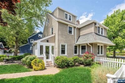 Traditional Ridgewood home with beige siding, a landscaped yard, and a white picket fence.