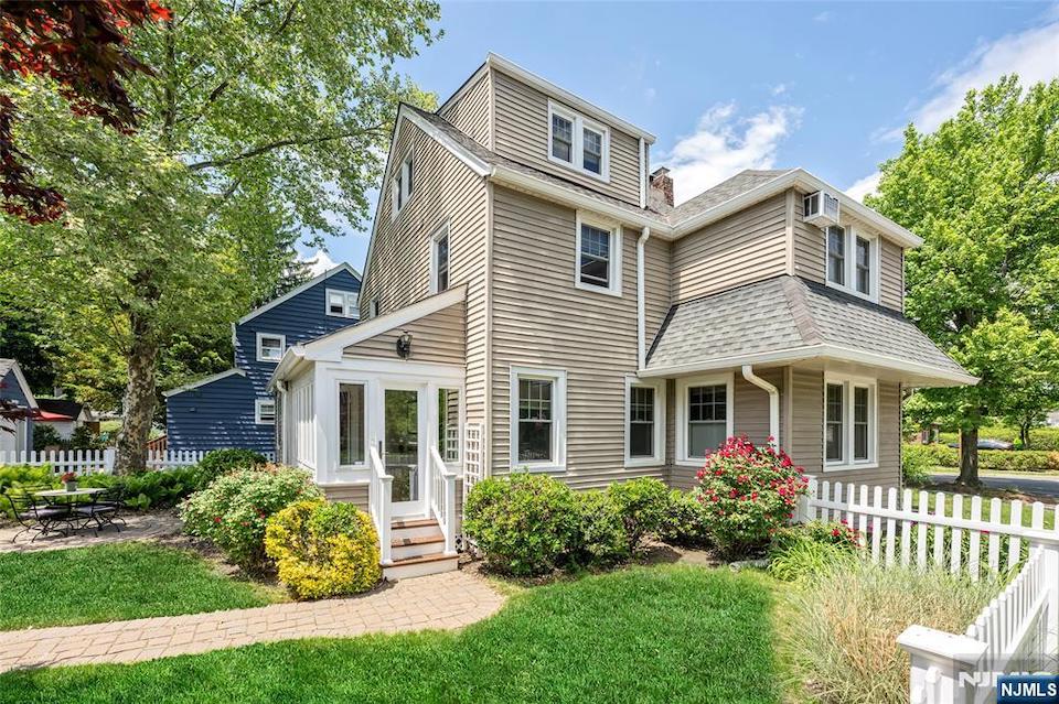 Traditional Ridgewood home with beige siding, a landscaped yard, and a white picket fence.